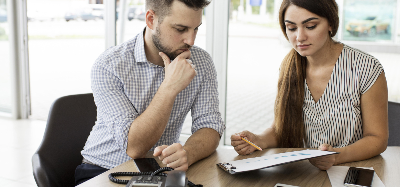 Dois colegas de trabalho analisam gráficos financeiros num escritório moderno, com tablet, telemóveis e telefone fixo sobre a mesa. Imagem que representa consultoria financeira e planeamento de crédito.